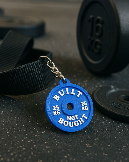 Blue weightlifting disc keychain with 'Built Not Bought' text on a gym floor background.