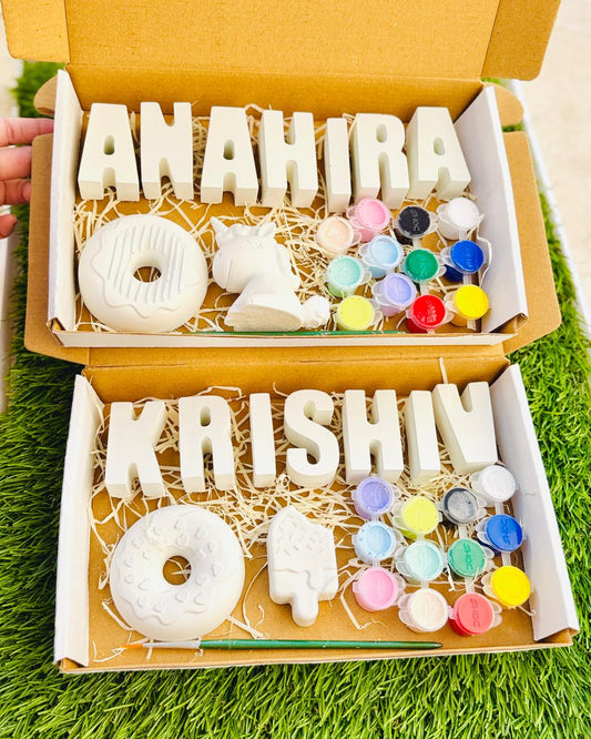 Decorative letters and small figurines in a box with 'ANAHIRA' and 'KRISHN' on a grassy background