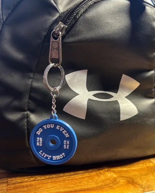 Black duffel bag with Under Armour logo and blue weightlifting plate keychain on a wooden surface.