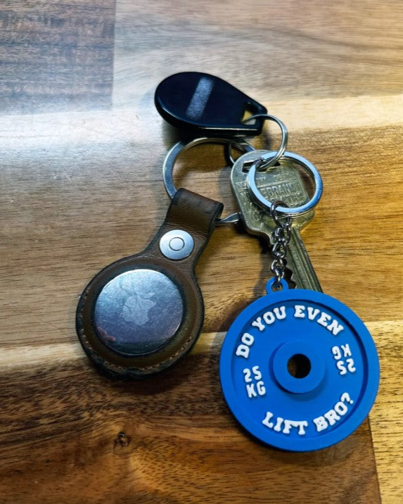Keychain with blue weightlifting disc and black leather case on wooden surface
