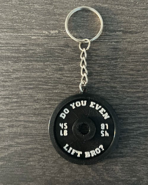 Black weightlifting disc keychain with humorous text on a wooden surface