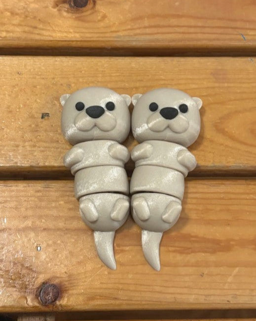 Two small gray otter figurines on a wooden surface