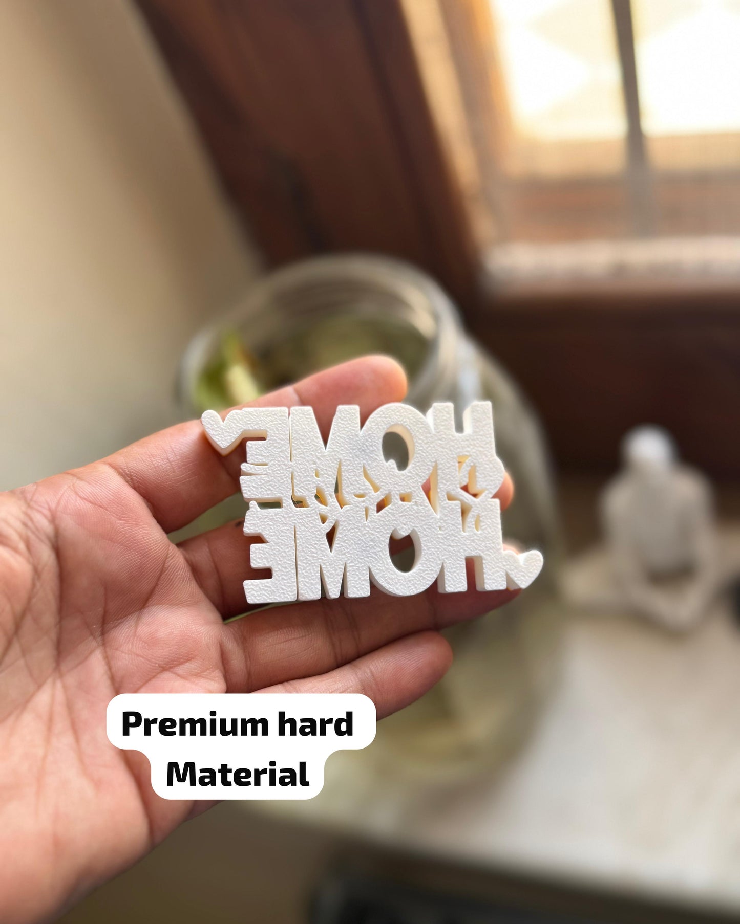 Hand holding a white decorative item with 'MOM' and 'DAD' text, blurred indoor background.
