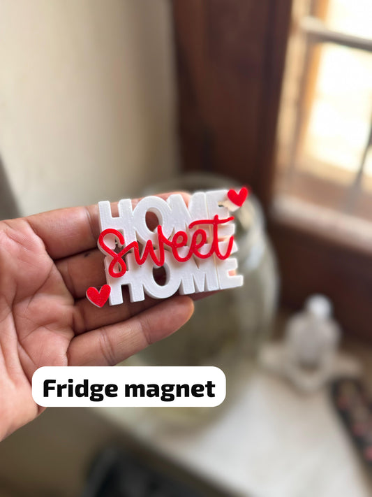 Fridge magnet with 'Home sweet home' text held in a hand, blurred background