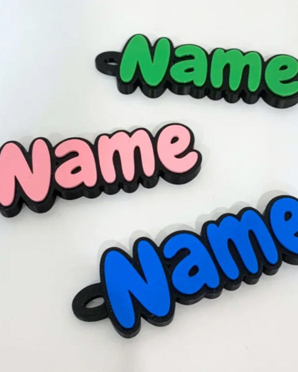 Three hair ties with 'Name' text in green, pink, and blue on a white background