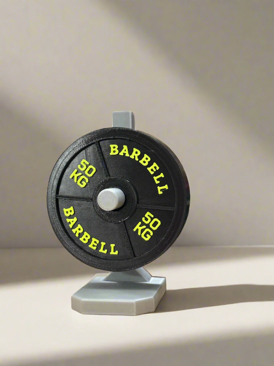 Barbell weight disc with '50 KG' marking on a stand, colorful spools in the background.