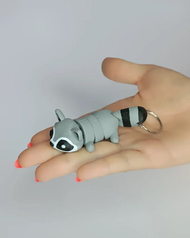 Hand holding a raccoon-shaped keychain against a plain background