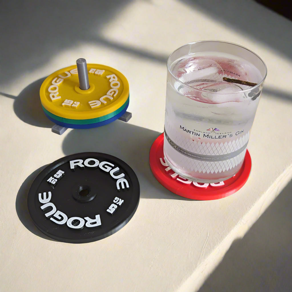Two weight plates and a glass of water with ice on a coaster, all branded with 'Rogue'.