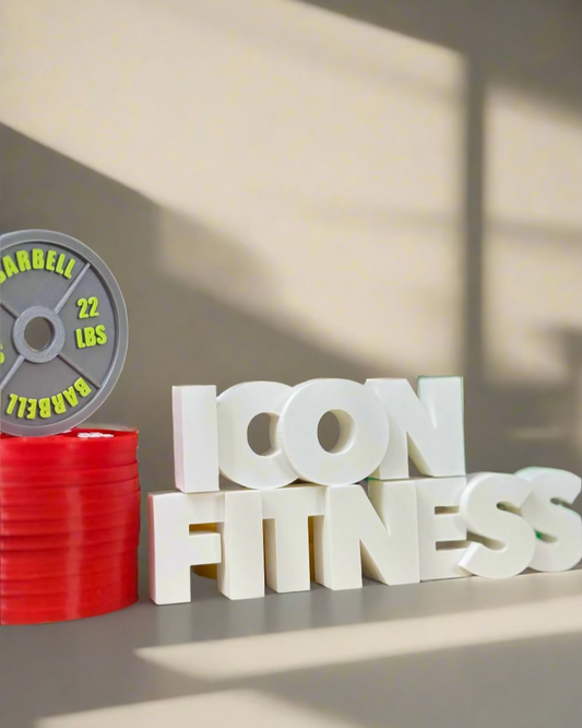 White 'ICON FITNESS' letters with red weights and gray barbell plate on a reflective surface.
