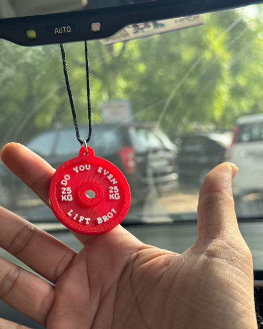 Red weightlifting disc charm held up in front of a car's rearview mirror.
