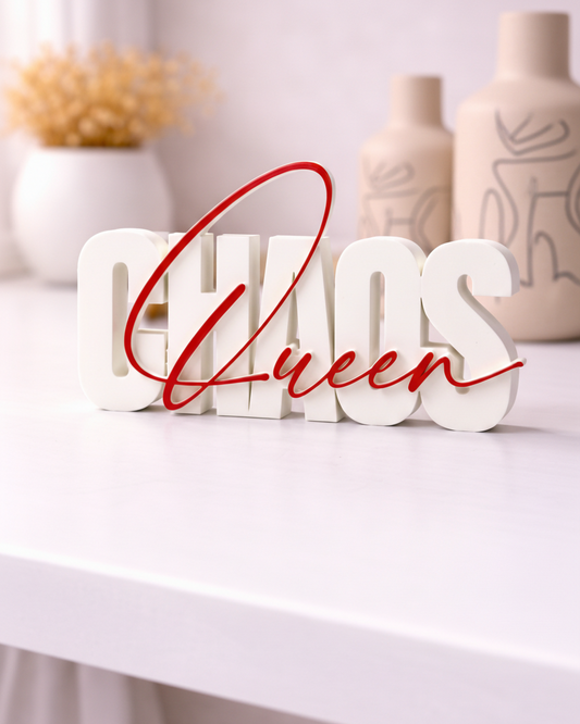 Decorative sign with 'Chaos Queen' text on a white surface with vases in the background
