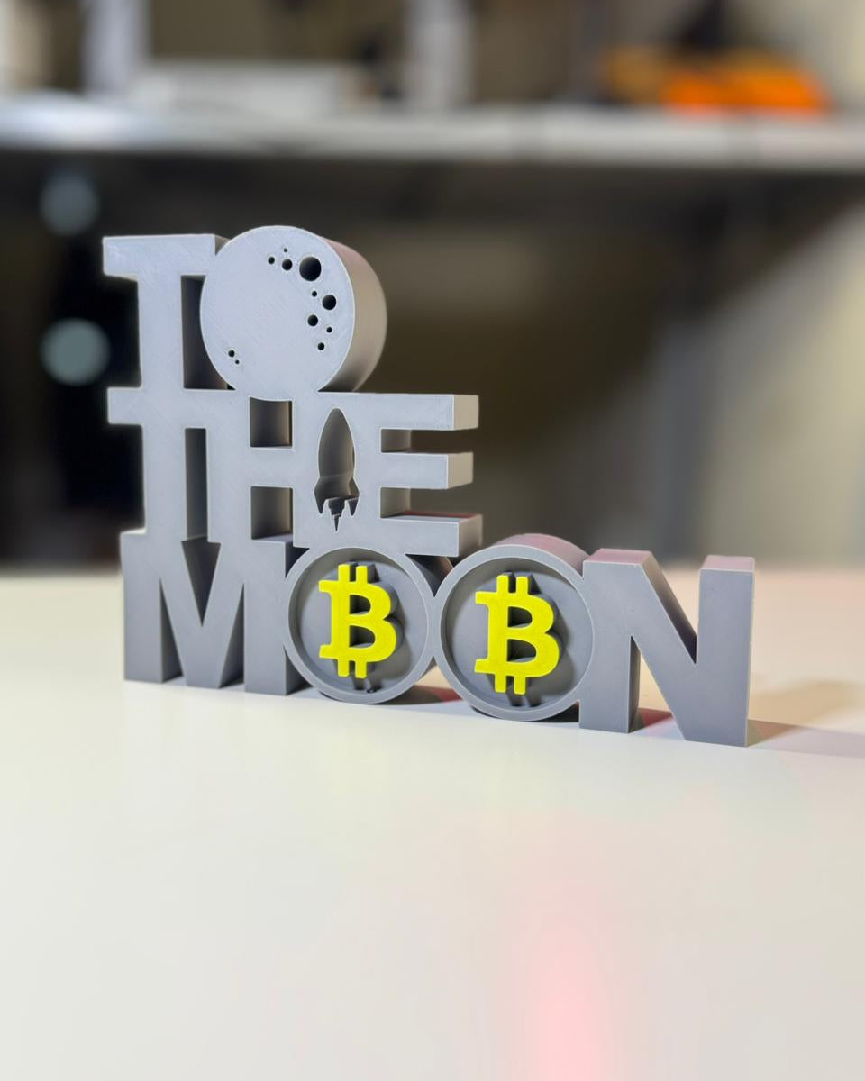 3D-printed Bitcoin-themed decorative piece with 'To the Moon' text on a blurred background