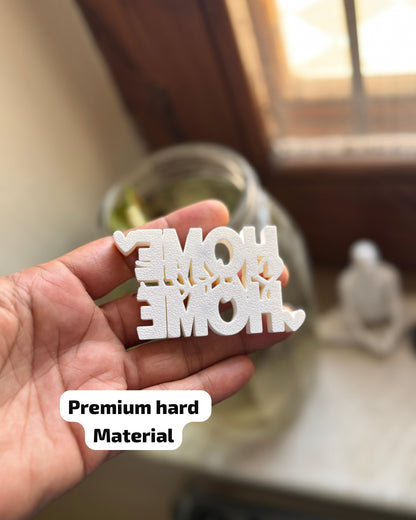 Hand holding a white decorative item with 'MOM' and 'DAD' text, blurred indoor background.