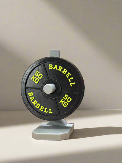 Barbell weight disc with '50 KG' marking on a stand, colorful spools in the background.