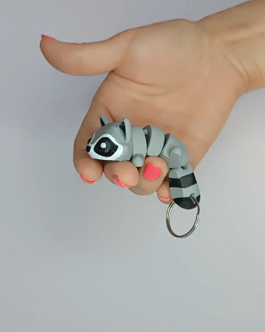 Hand holding a raccoon-shaped keychain against a plain background