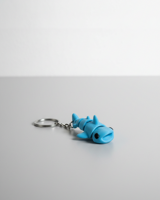 Blue shark-shaped keychain on a light gray surface with a white background