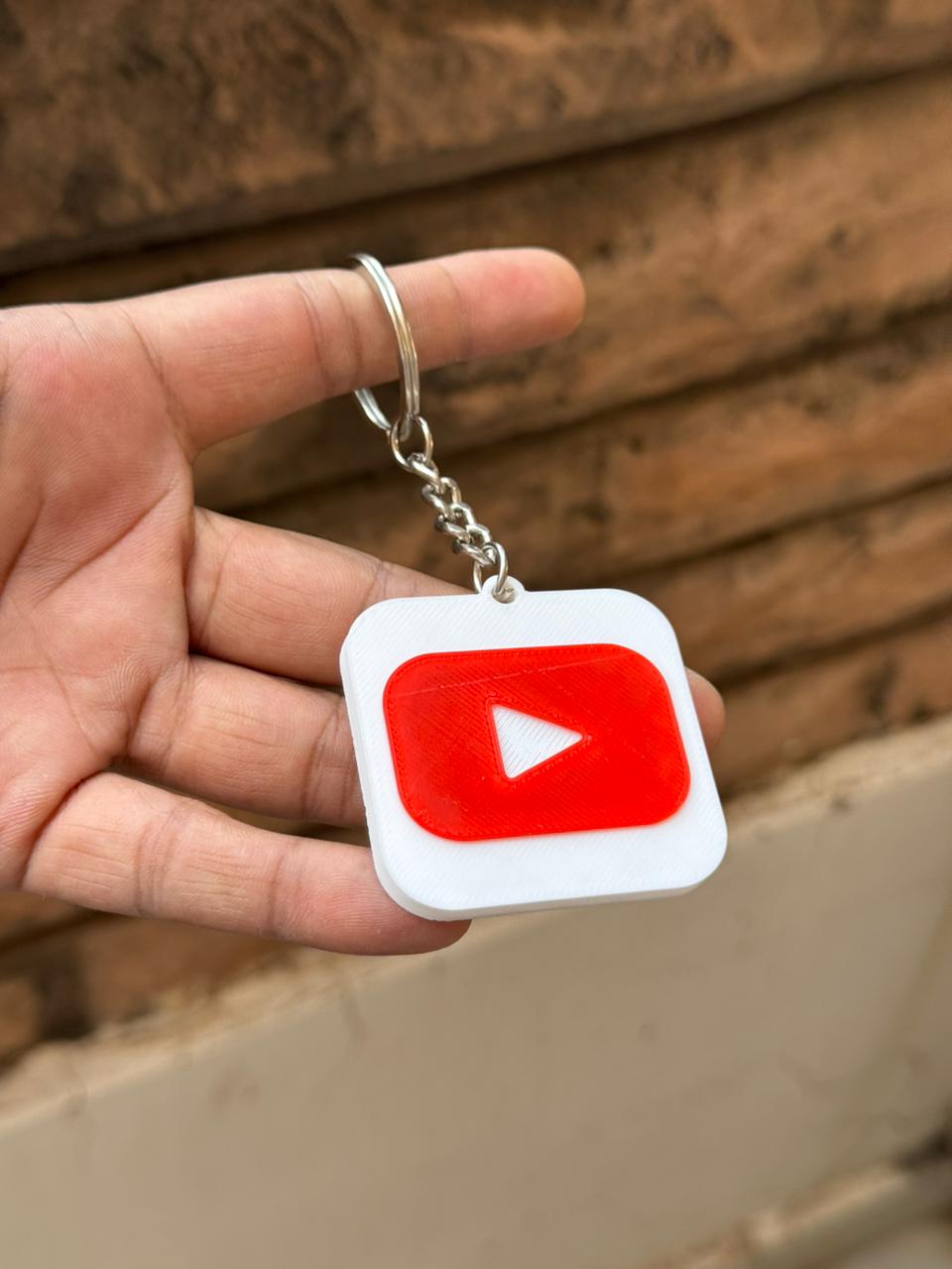 Hand holding a keychain with a YouTube logo against a wooden background